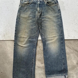 May include: Faded blue denim jeans with a straight leg cut. The jeans show signs of wear and tear, with lighter patches and a worn-in look. Classic five-pocket design with a button and zip closure.