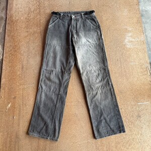 Puede incluir: Vaqueros grises con diseño de patchwork. Los vaqueros tienen cierre de botón y cremallera, trabillas para el cinturón y pernera recta. El denim tiene un aspecto descolorido, con parches más oscuros en las rodillas y muslos.