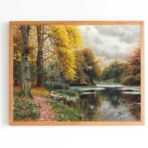 Könnte beinhalten: Ein gerahmtes Ölgemälde, das eine ruhige Herbstszene zeigt. Ein kleines Boot liegt am Rande eines stillen Sees, umgeben von Bäumen mit leuchtend gelben Blättern. Der Himmel ist mit weichen, grauen Wolken bedeckt.