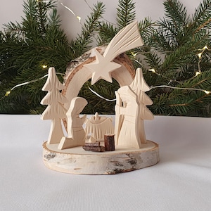 Puede incluir: Un belén de madera con una estrella y un cometa tallados en la base de madera de abedul. La escena incluye tres figuras, un árbol y un pesebre.