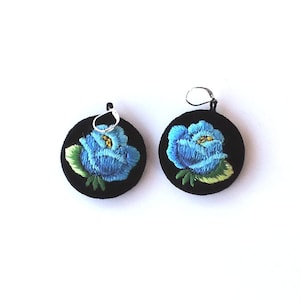 Pode incluir: Um par de brincos com flores azuis bordadas em círculos de feltro preto com ganchos prateados.
