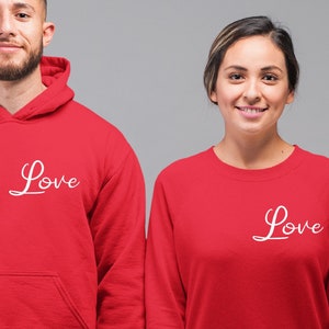 Può includere: Due felpe rosse con la parola "Love" scritta in corsivo bianco sul davanti. La felpa a sinistra è una felpa con cappuccio, e la felpa a destra è una felpa a collo rotondo.