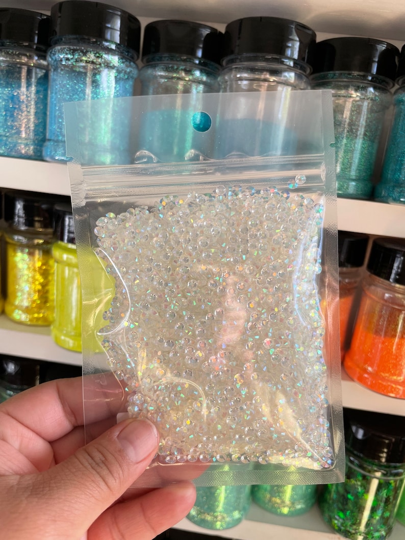 May include: A clear plastic bag filled with iridescent white round beads. The bag is sealed and has a hole at the top for hanging.