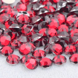 May include: A large quantity of small, red, round rhinestones. The rhinestones have a faceted, crystal-like appearance.