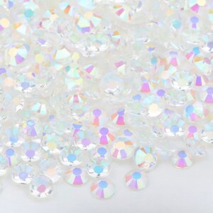 May include: A pile of iridescent clear glass rhinestones. The rhinestones are round and have a faceted design.