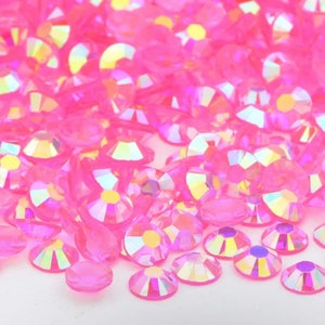 May include: A large pile of iridescent pink rhinestones. The rhinestones are scattered on a white surface.