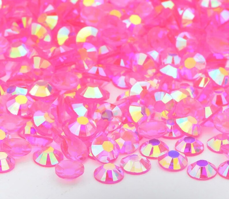 May include: A large pile of iridescent pink rhinestones. The rhinestones are scattered on a white surface.