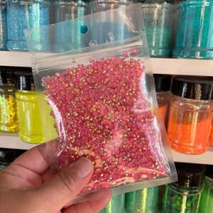 May include: A clear plastic bag filled with iridescent pink glitter. The glitter is in a small, round shape and is perfect for crafting projects.