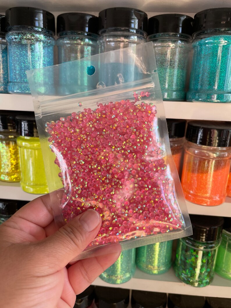 May include: A clear plastic bag filled with iridescent pink glitter. The glitter is in a small, round shape and is perfect for crafting projects.
