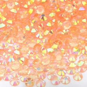 May include: A close-up view of a large quantity of small, round, iridescent peach-colored rhinestones.