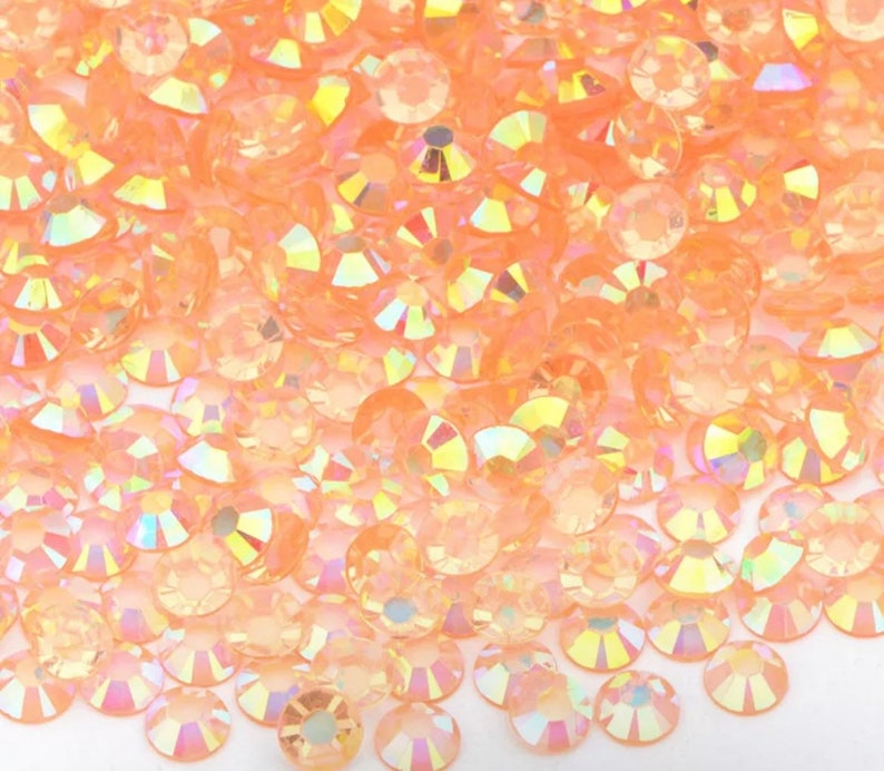May include: A close-up view of a large quantity of small, round, iridescent peach-colored rhinestones.