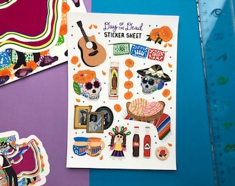 May include: A sticker sheet with a Day of the Dead theme. The sheet includes stickers of a guitar, sugar skulls, marigolds, a traditional Mexican bread, a doll, and bottles of hot sauce. The text "Day of the Dead Sticker Sheet" is printed at the top of the sheet.