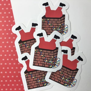 Puede incluir: Una colección de pegatinas con Santa Claus atascado en una chimenea. La chimenea es de ladrillos marrones, y se ven el traje rojo y las botas negras de Santa. Luces navideñas de colores envuelven la chimenea.