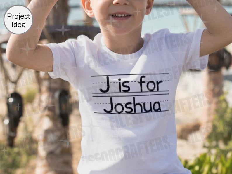 Puede incluir: Una camiseta blanca con texto negro que dice "J es para Joshua" sobre un fondo rayado. La camiseta la lleva puesta un ni&ntilde;o.