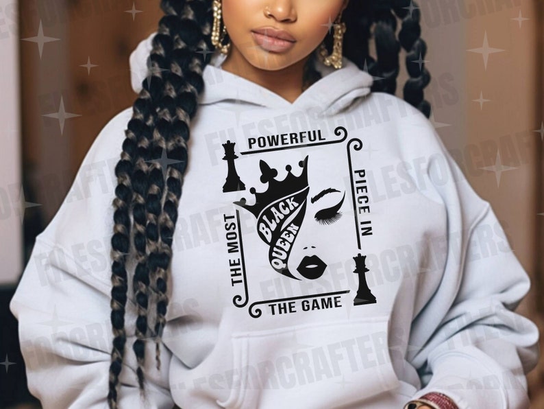 Puede incluir: Sudadera blanca con un dise&ntilde;o gr&aacute;fico negro que presenta una pieza de ajedrez de reina con una corona y el texto "The Most Powerful Piece In The Game" y "Black Queen".