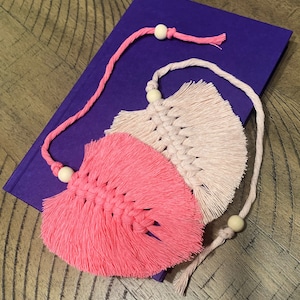 May include: Two pink and beige macrame feather-shaped tassels with wooden beads attached to a string.