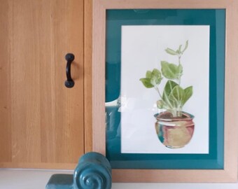 May include: A framed watercolor painting of a potted plant with green leaves and a brown pot with a colorful glaze. The frame is light wood with a teal mat.