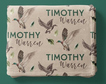 May include: A beige fleece blanket with a repeating pattern of flying ducks and green leaves. The text "TIMOTHY Warren" is repeated throughout the blanket.