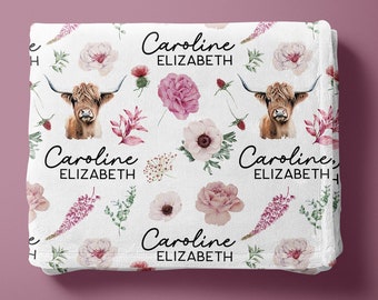 May include: White baby blanket with a floral pattern featuring pink and white flowers, green leaves, and brown Highland cows. The blanket has the name "Caroline Elizabeth" repeated four times.