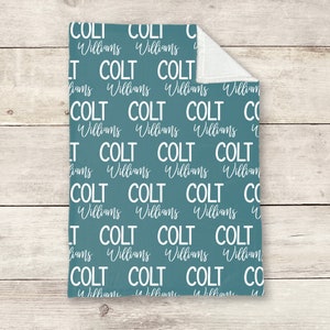 May include: A teal blue baby blanket with the name "Colt Williams" repeated in white text.