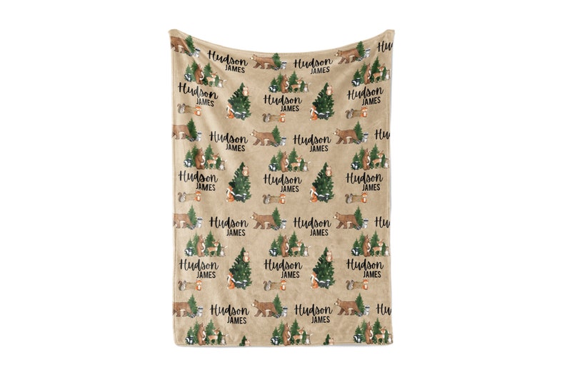 Puede incluir: Una manta de franela marr&oacute;n con un patr&oacute;n repetido de animales del bosque, &aacute;rboles y el texto "Hudson James".