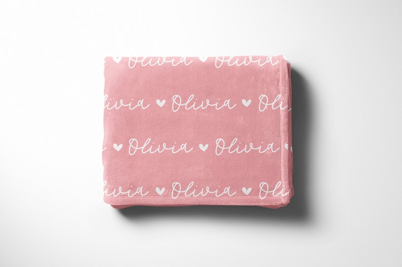 May include: A pink fleece blanket with the name "Olivia" repeated in white script with small white hearts between each name.