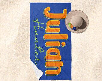 May include: A blue beach towel with the name "Julian" written in orange and yellow letters with a green outline. The text "Hunter" is written in green cursive below the name.