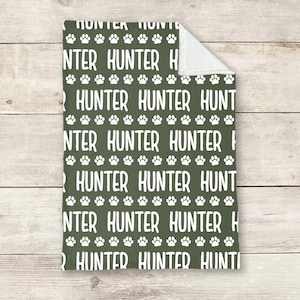 May include: A green fleece blanket with a white paw print and the name "Hunter" repeated in a pattern.