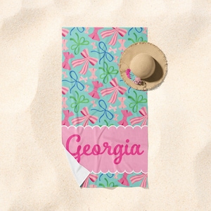 May include: A turquoise beach towel with a pink and green bow pattern. The towel has a pink banner with the name "Georgia" written in pink.