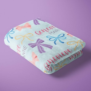 May include: A light blue blanket with a pattern of colorful bows and the names Genevieve Mari, Genevieve, and Janine.