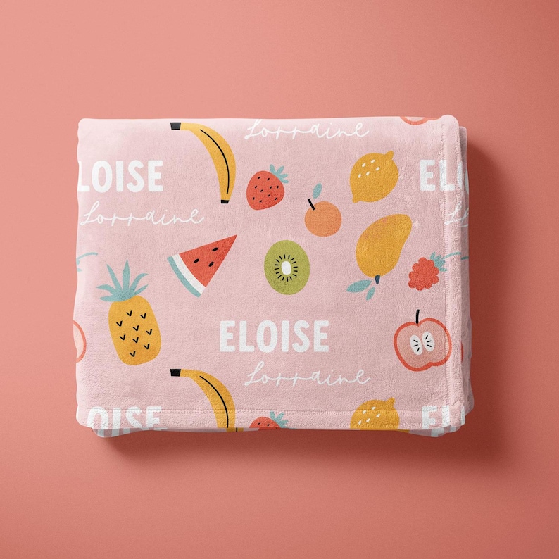 May include: Pink fleece blanket with a colorful fruit pattern and the name "Eloise" repeated throughout. The blanket is perfect for a child's room.
