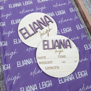 May include: Two wooden baby announcement plaques with the name "Eliana Leigh" in purple lettering. The smaller plaque has spaces to record the baby's date, time, weight in pounds and ounces, and length in inches.