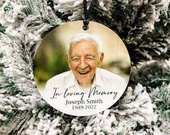 May include: A round, white ornament with a photo of a smiling man. The ornament has black text that reads "In loving memory Joseph Smith 1949-2022".