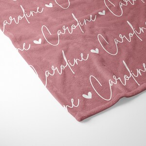 May include: A soft, pink fleece blanket with the name "Caroline" repeated in white script with white hearts in between each name.