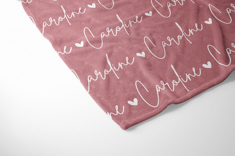 May include: A soft, pink fleece blanket with the name "Caroline" repeated in white script with white hearts in between each name.