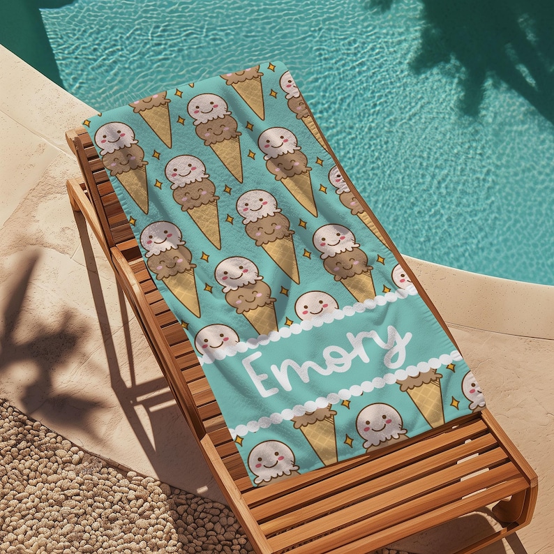 May include: A turquoise beach towel with a repeating pattern of ice cream cones. The ice cream cones are brown and white with a smiling face. The towel has the name "Emory" written in white on a turquoise banner.