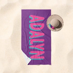 May include: Purple beach towel with the name "ADALYN" in pink and teal letters.