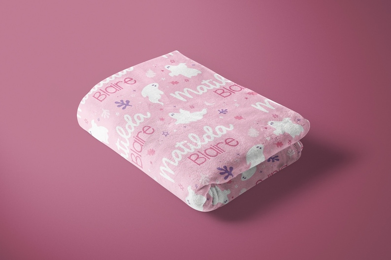 K&ouml;nnte beinhalten: Eine rosa Babydecke mit einem wei&szlig;en Geistermuster und den Namen "Blair" und "Matilda", die sich &uuml;ber die gesamte Oberfl&auml;che wiederholen.
