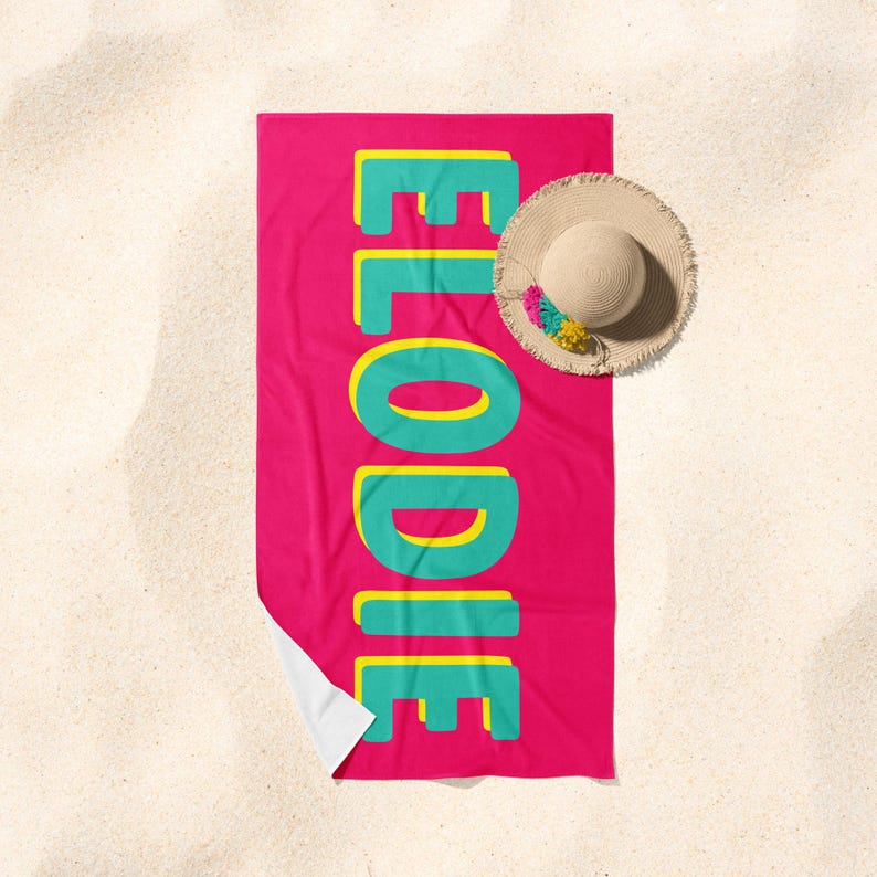 May include: A pink beach towel with the name "Elodie" written in large, turquoise letters outlined in yellow.