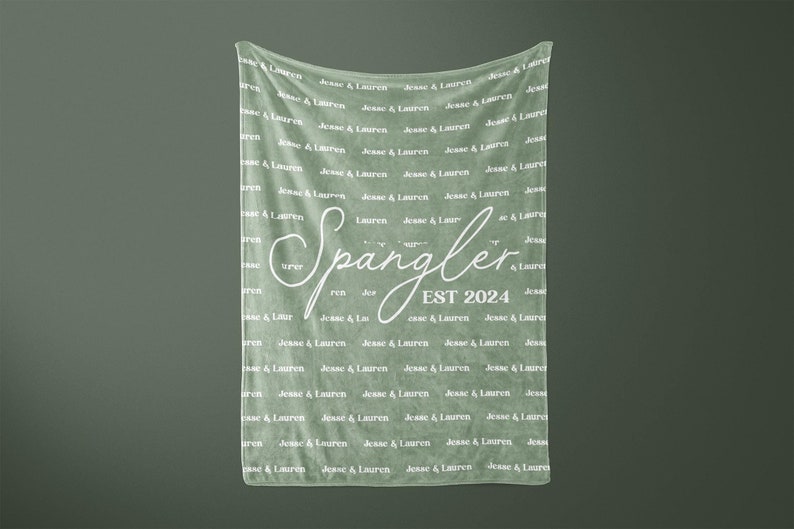 May include: A sage green fleece blanket with the text "Spangler EST 2024" in white cursive lettering. The blanket is covered in the repeated text "Jesse & Lauren" in white.