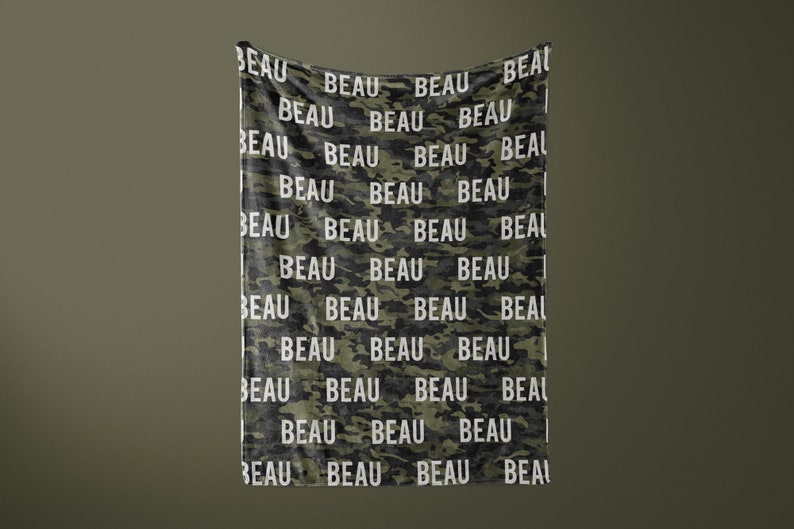 K&ouml;nnte beinhalten: Eine gr&uuml;n-schwarze Tarnmuster-Decke mit dem Namen "BEAU", der in wei&szlig;er Schrift wiederholt wird.
