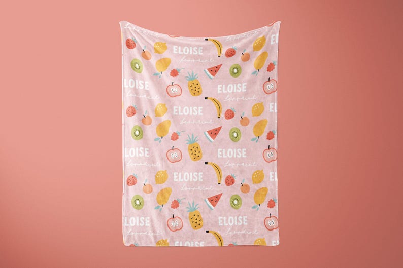 May include: Pink baby blanket with a repeating pattern of fruit, including pineapples, lemons, bananas, watermelons, kiwi, and apples. The text "ELOISE loves fruit" is repeated throughout the blanket.