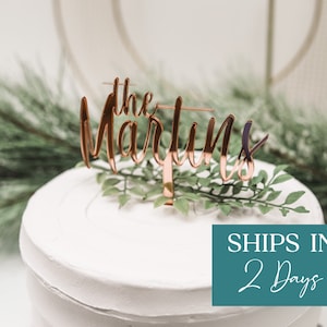 May include: A white cake with a rose gold cake topper that says "the Martins".