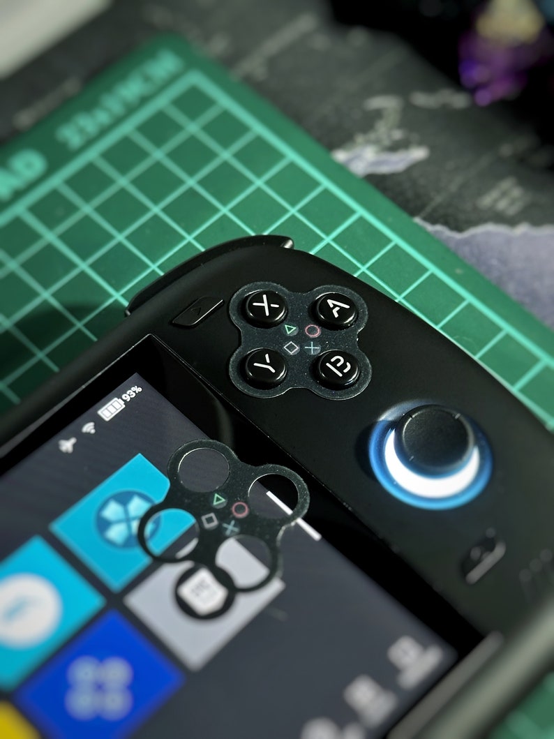 Op de afbeelding: Een zwart draagbaar gameapparaat met een groene en zwarte achtergrond. Het apparaat heeft een scherm, knoppen en een joystick. Het scherm toont een blauw en wit pictogram.