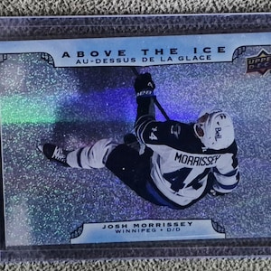 May include: A hockey trading card featuring Josh Morrissey of the Winnipeg Jets. The card has a holographic background with the text "ABOVE THE ICE" and "AU-DESSUS DE LA GLACE". The Upper Deck logo is visible.