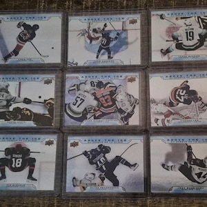 May include: Nine hockey trading cards in protective sleeves. Each card shows a hockey player in action on the ice. The cards have the text "ABOVE THE ICE" and player names. The players are wearing hockey uniforms.