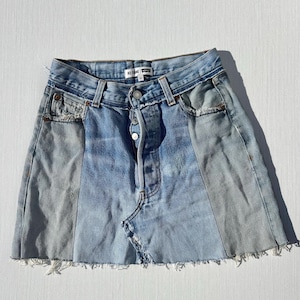 May include: A blue denim skirt with a raw hem and a contrasting panel of lighter denim. The skirt has a button fly and a high waist. The brand label reads "RE/DONE" and "Levi's".