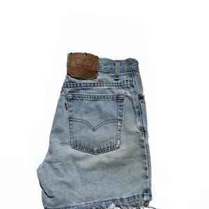 May include: Light blue denim shorts with frayed edges and a brown leather patch on the back. The patch has the text "Levi's" and other text in white.