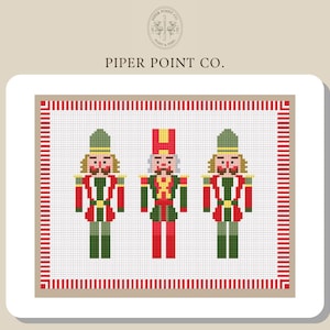 Puede incluir: Un diseño de punto de cruz con tres cascanueces de juguete en rojo, verde y dorado. Los cascanueces están en fila, cada uno con un sombrero diferente. El diseño está enmarcado con un borde rojo y blanco. El texto "PIPER POINT CO." está en la parte superior.
