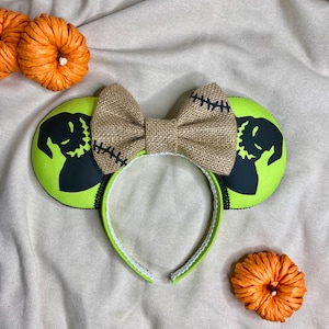 May include: Green and black mouse ears with a burlap bow. The ears feature a silhouette of Jack Skellington from The Nightmare Before Christmas.
